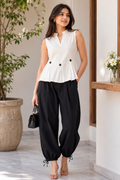 Woman wearing a white sleeveless top and black pants, standing indoors.