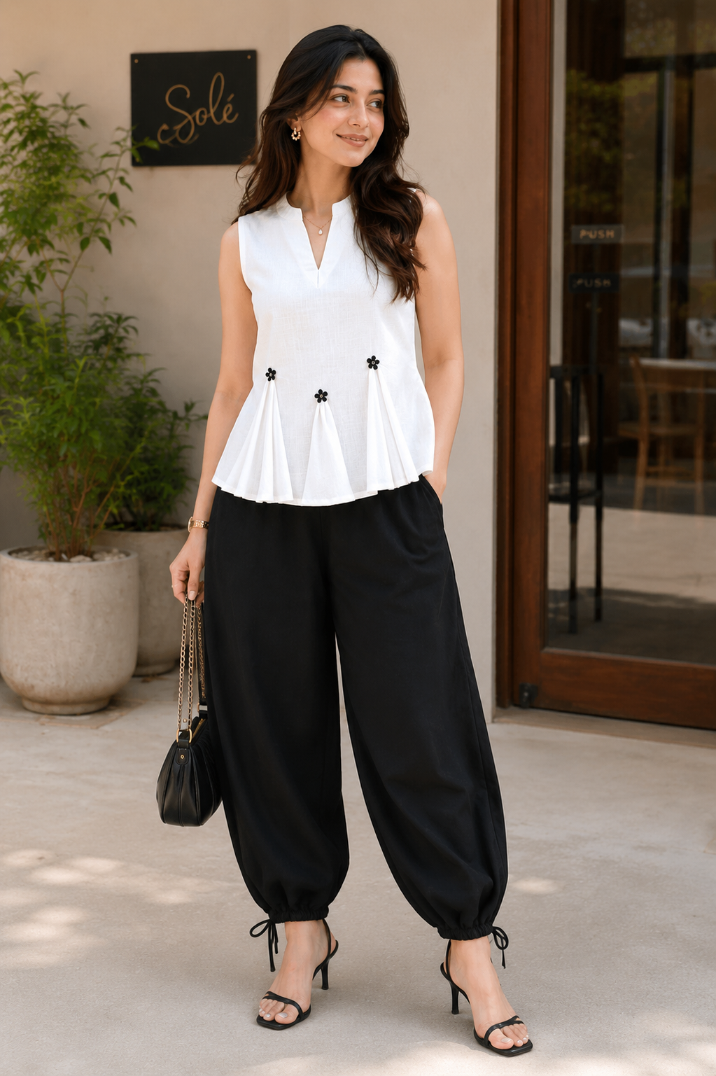 Woman wearing a white sleeveless top and black wide-leg pants, standing outdoors.